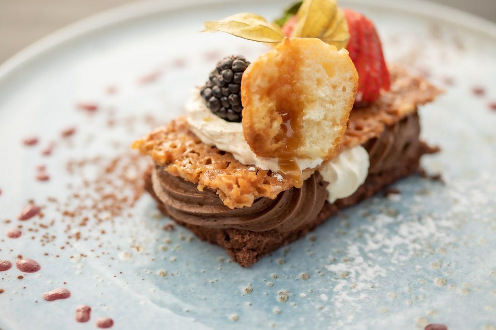 Chocolate dessert topped with fresh berries, whipped cream and caramelized garnish on blue plate.