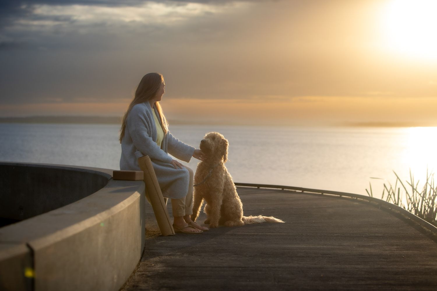 Golden retriever and companion sit peacefully on a dock at sunset overlooking a serene lake.