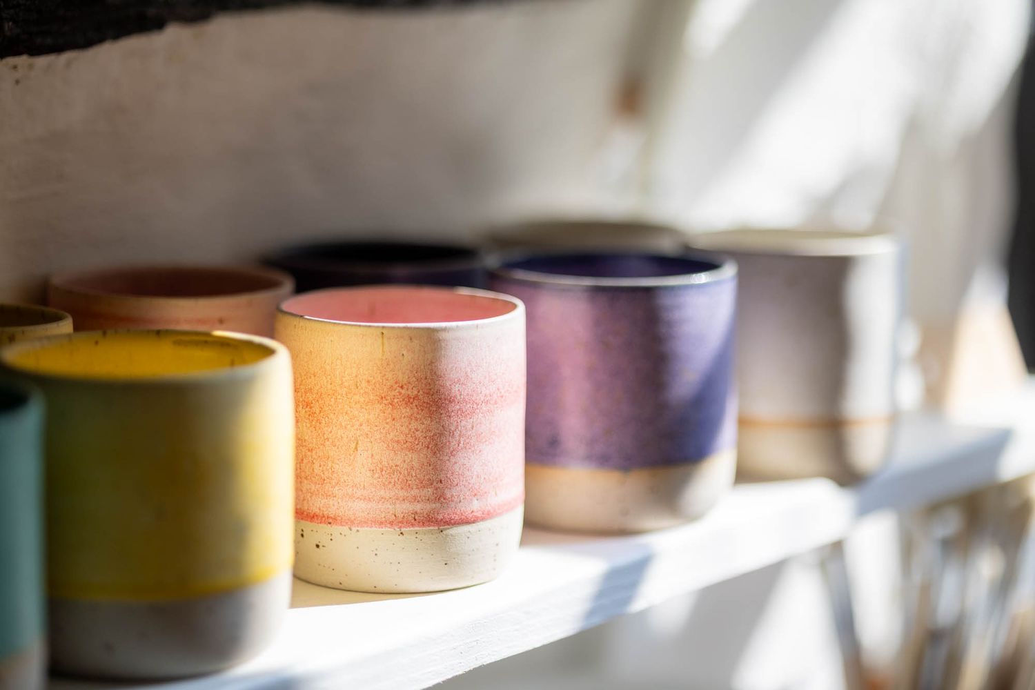 Colorful ceramic cups arranged on shelf showing gradient of yellow, orange, and purple glazes.