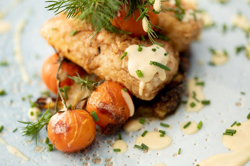 Pan-seared fish fillet with roasted cherry tomatoes and fresh herbs in a creamy sauce.