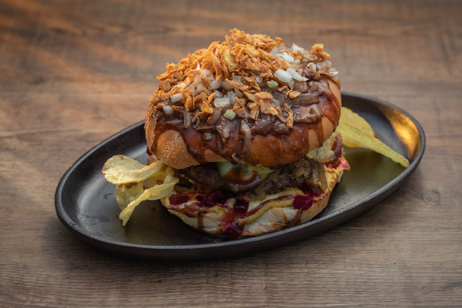 Gourmet sandwich with crispy toppings served on black oval platter.