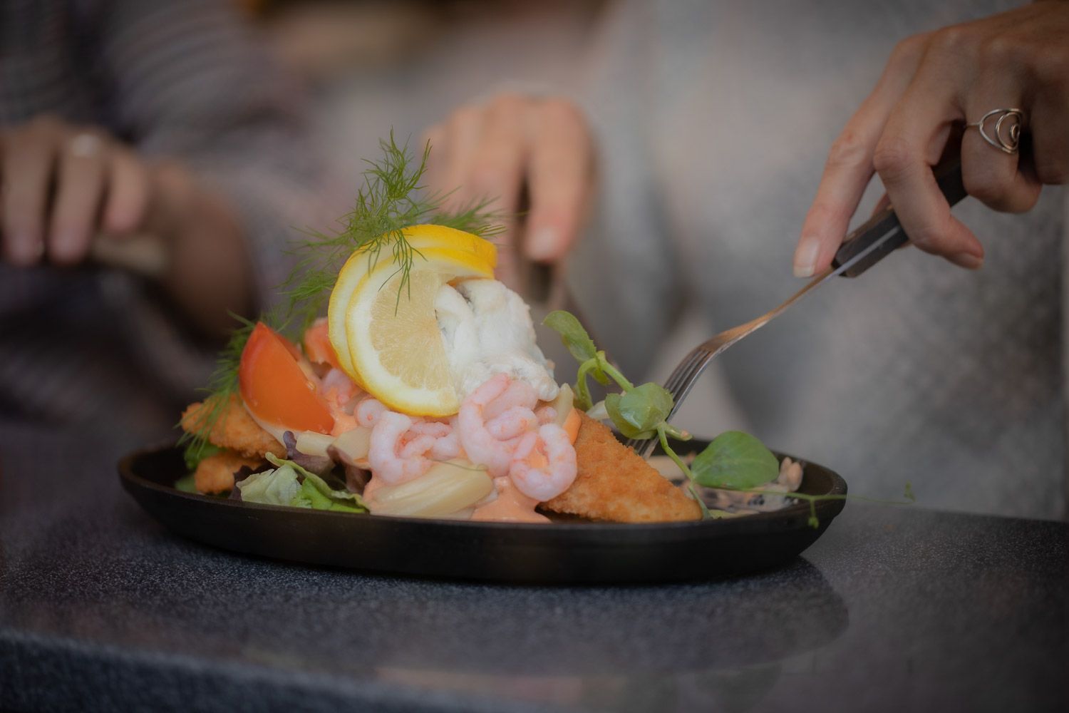 Seafood dish with lemon garnish and fresh herbs being plated.