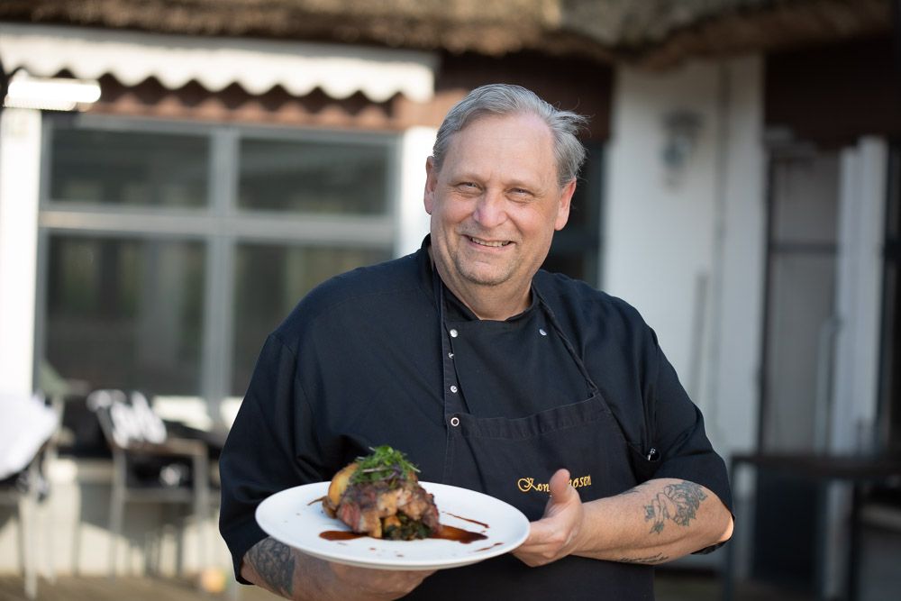 Chef presenting a plated gourmet dish outdoors at restaurant patio.