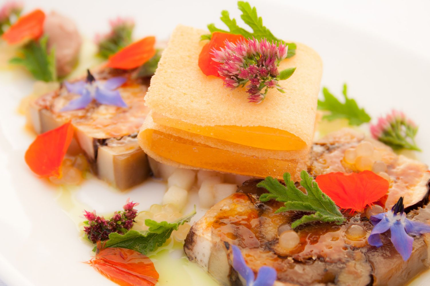Artistically plated seafood dish with colorful garnishes and edible flowers on white plate.