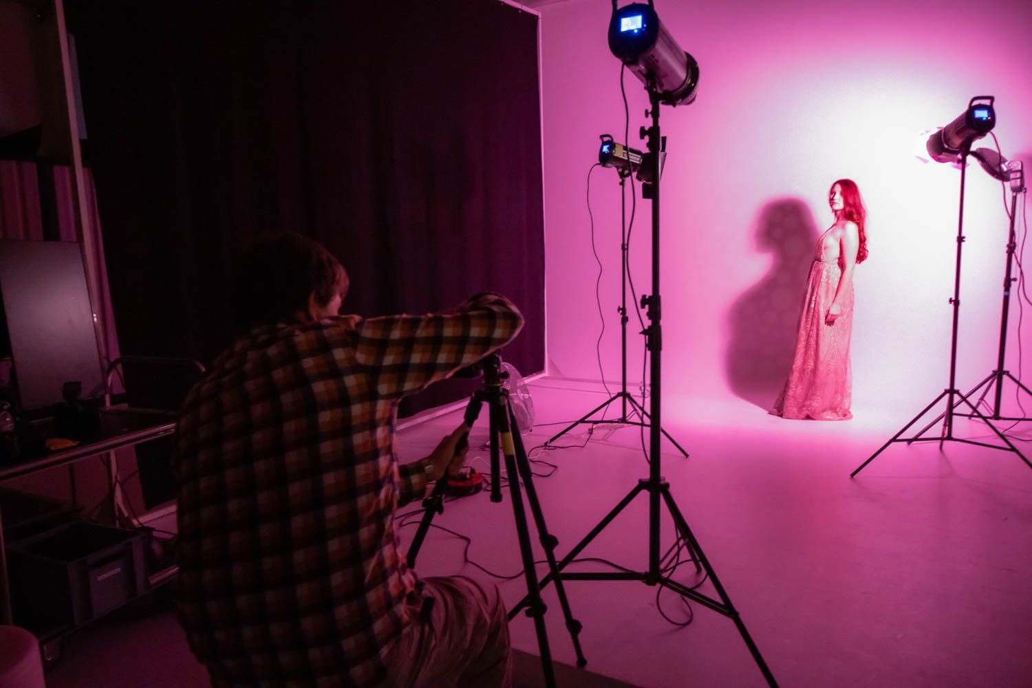 Professional photographer captures model in pink studio setting with multiple studio lights and equipment.