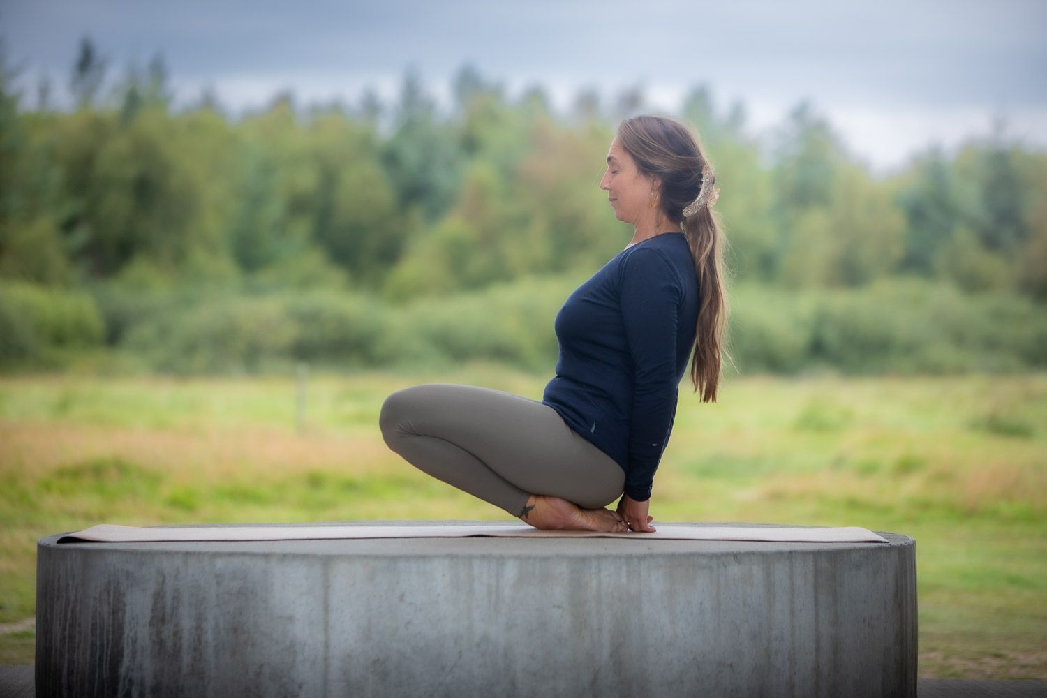 Person practicing yoga poses on concrete platform in natural setting.