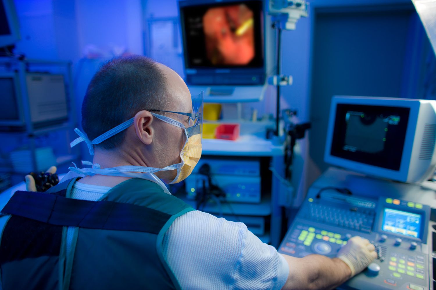 Medical team monitoring surgical procedure on digital displays in dimly lit operating room.