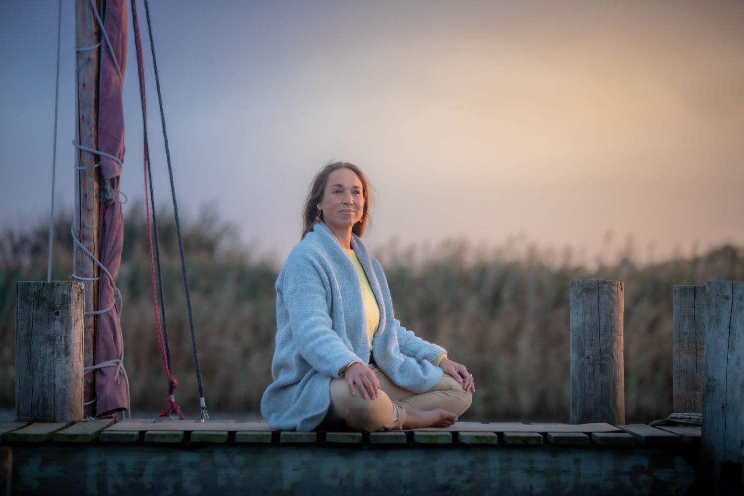 Person sitting on wooden deck railing at sunset in peaceful outdoor setting.