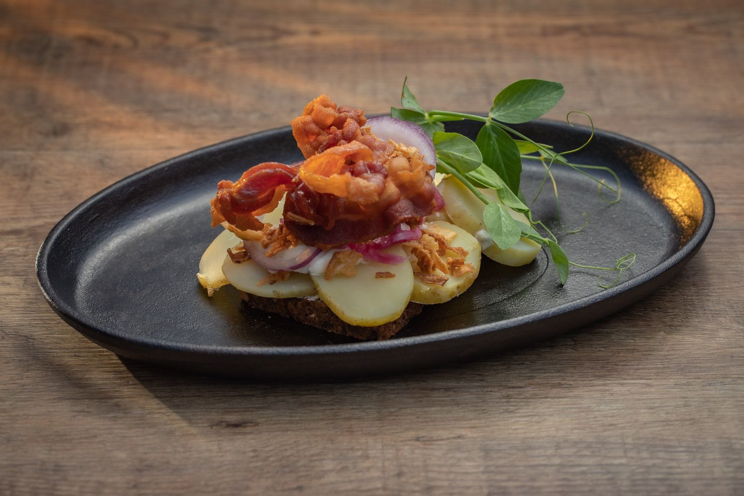 Gourmet appetizer served on black slate plate with fresh herbs and sauce.