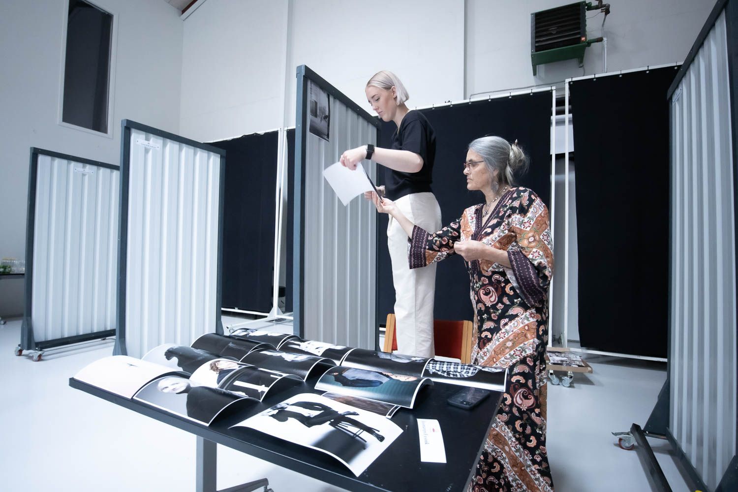 Two people reviewing photographic prints laid out on a table in a studio setting.
