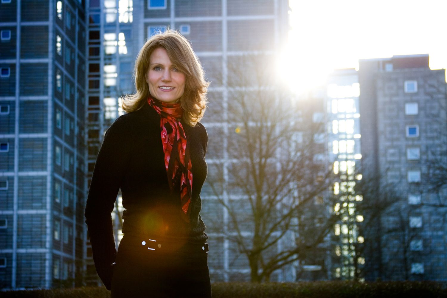 Outdoor portrait with urban architecture and sunlight in background.