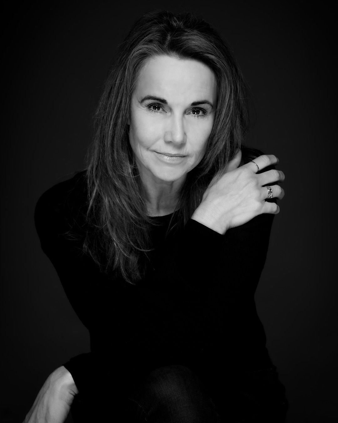 Black and white portrait of woman in dark sweater with long hair against black background.
