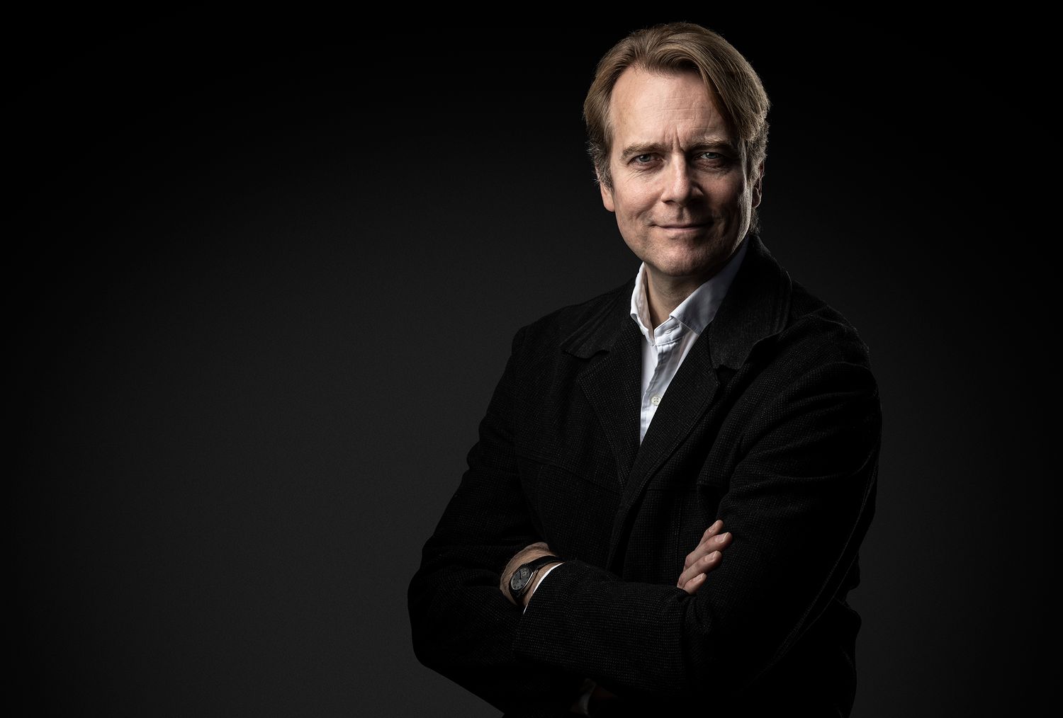 Business portrait of person in black jacket with arms crossed against dark background.