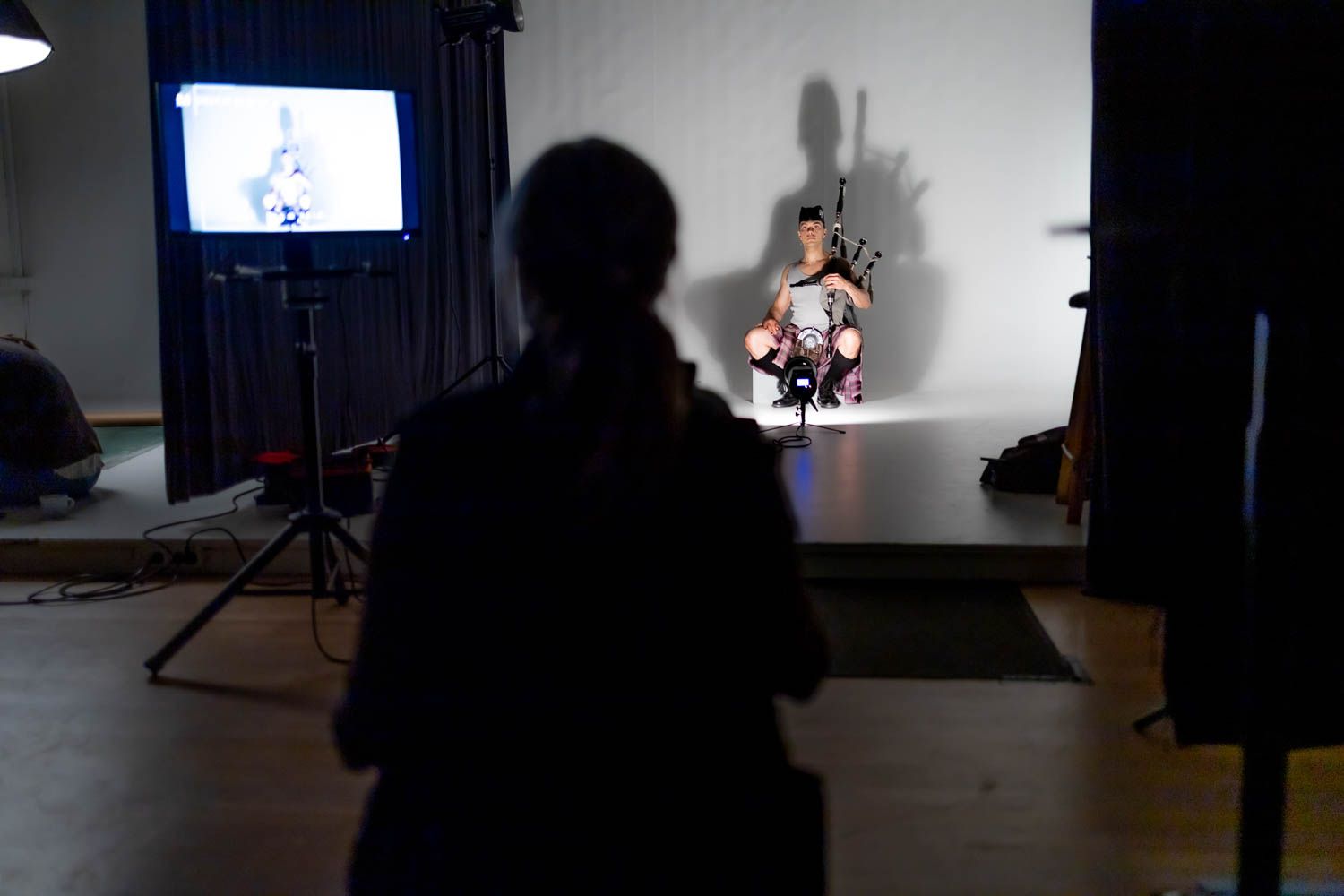 Dark studio space with lighting equipment and silhouettes visible during photo shoot setup.