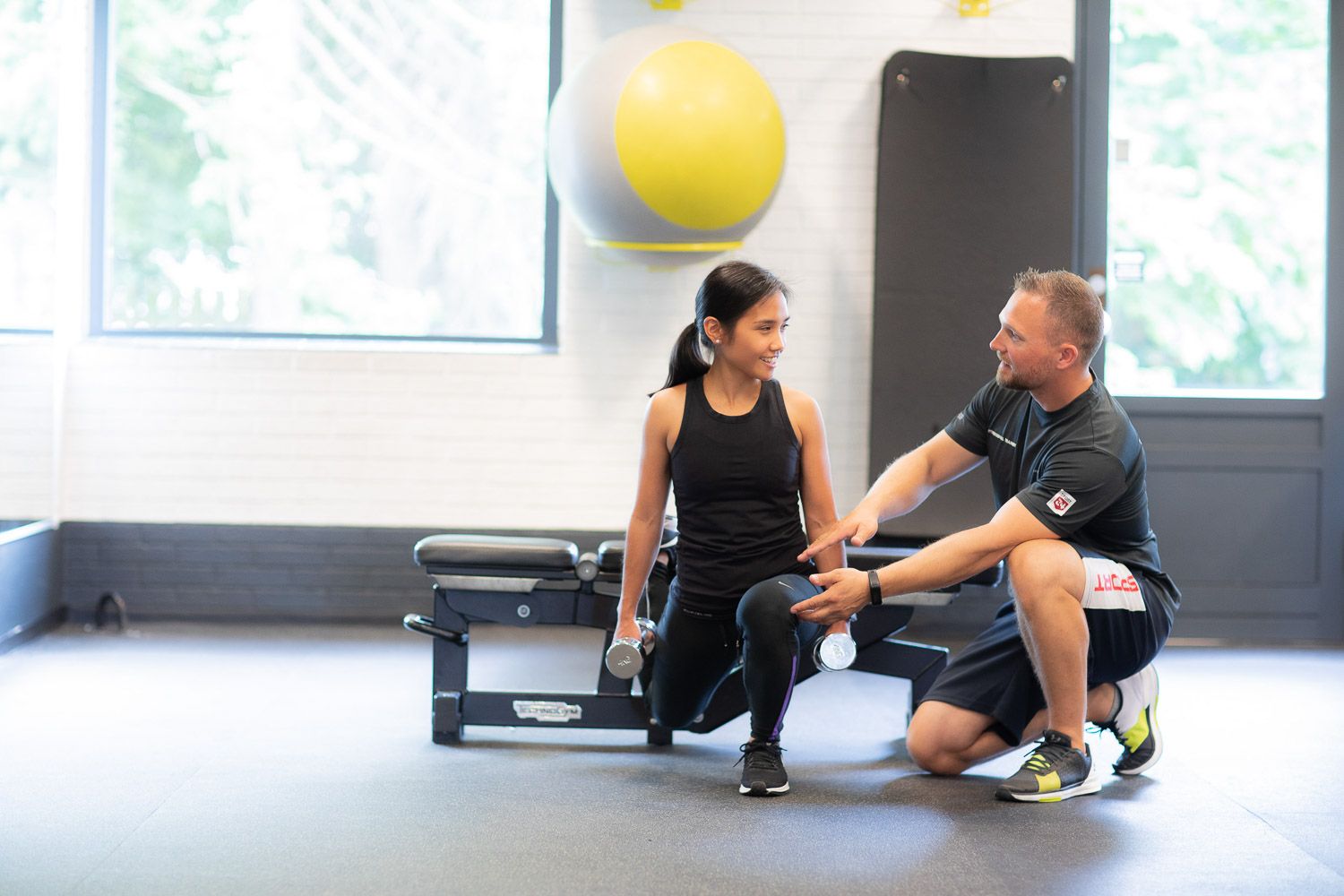 Professional trainer working with client on proper exercise technique in modern gym setting.