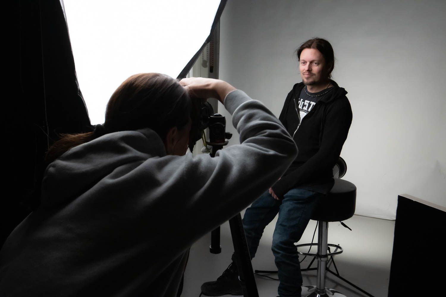 Dramatic black and white studio portrait session showing lighting setup and photographer silhouette.