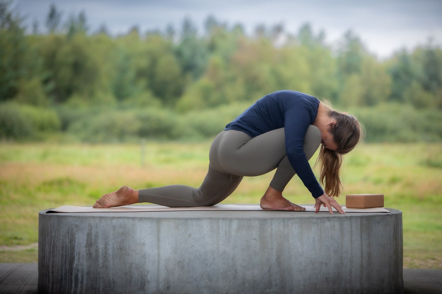 Person practicing yoga stretches and poses on an outdoor concrete platform.