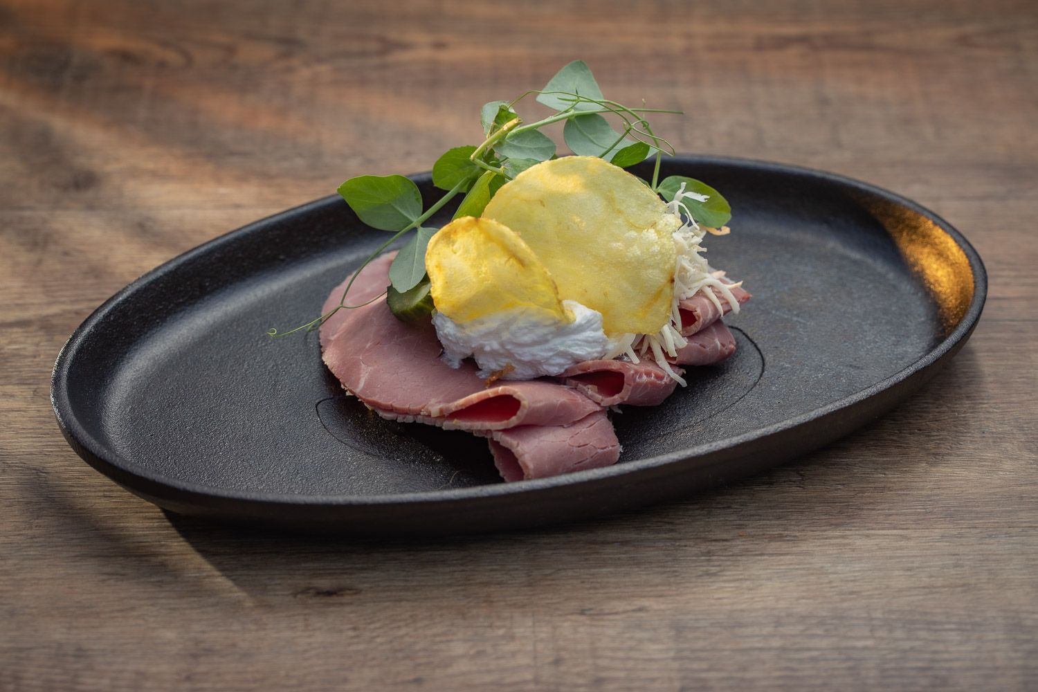 Elegantly plated seafood dishes on black plates arranged on a rustic wooden table surface.