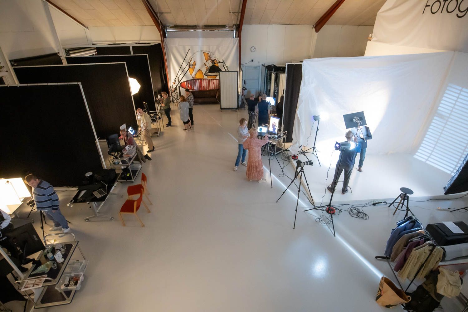 Wide angle view of professional photo studio with lighting equipment and white backdrop.