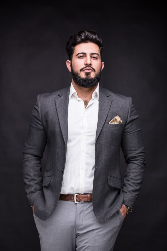 Business portraits of person in grey suit and white shirt against dark backdrop.