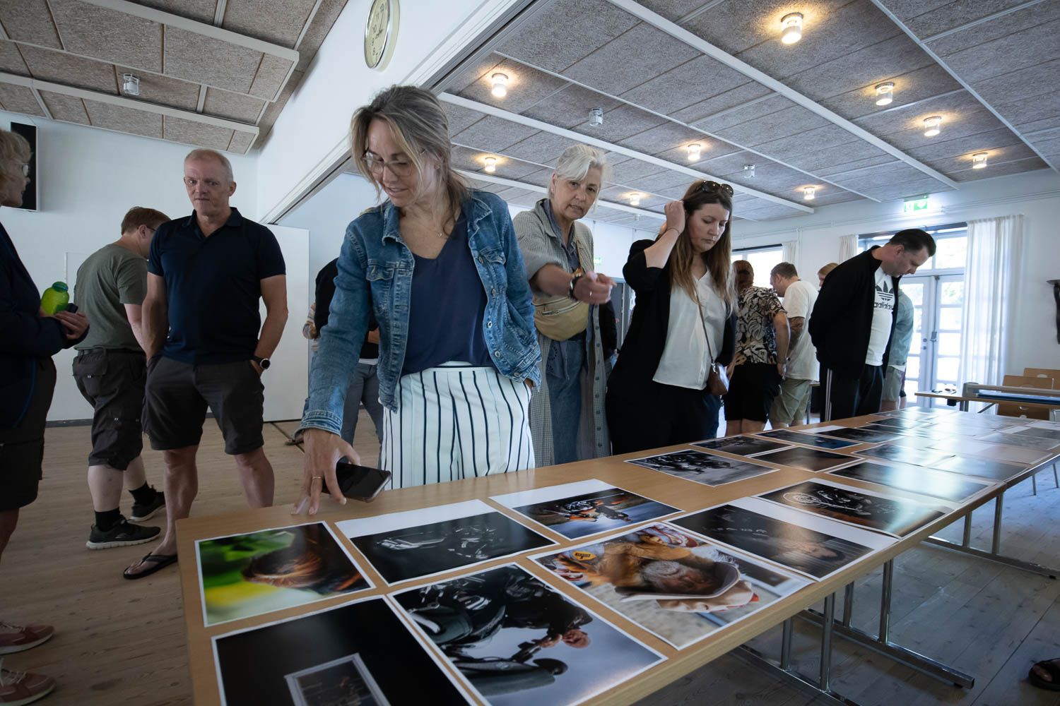 Group of people examining photographs laid out on long table during review session.