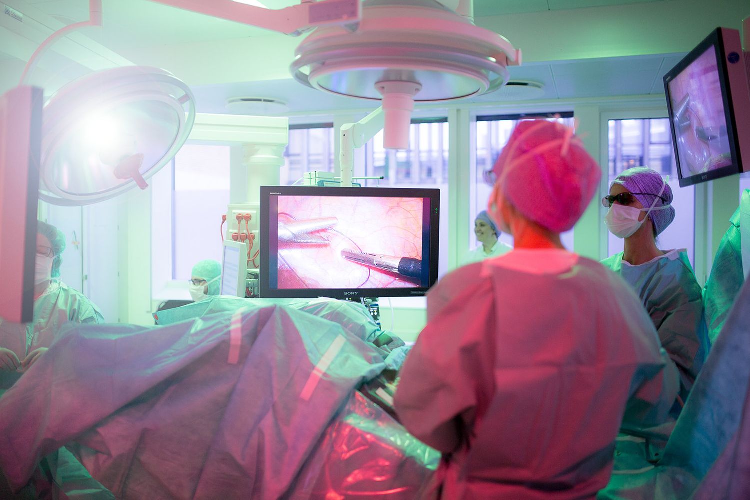 Hospital operating theater with medical staff performing surgery under colored lighting.