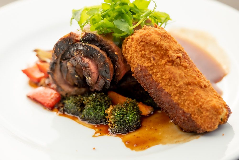 Gourmet plate featuring breaded meat cutlet with broccoli, greens and a dark sauce garnish.