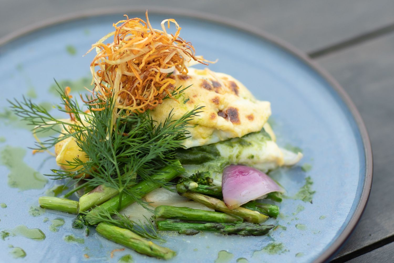 Fresh asparagus dish topped with crispy shredded garnish and dill on a blue ceramic plate.