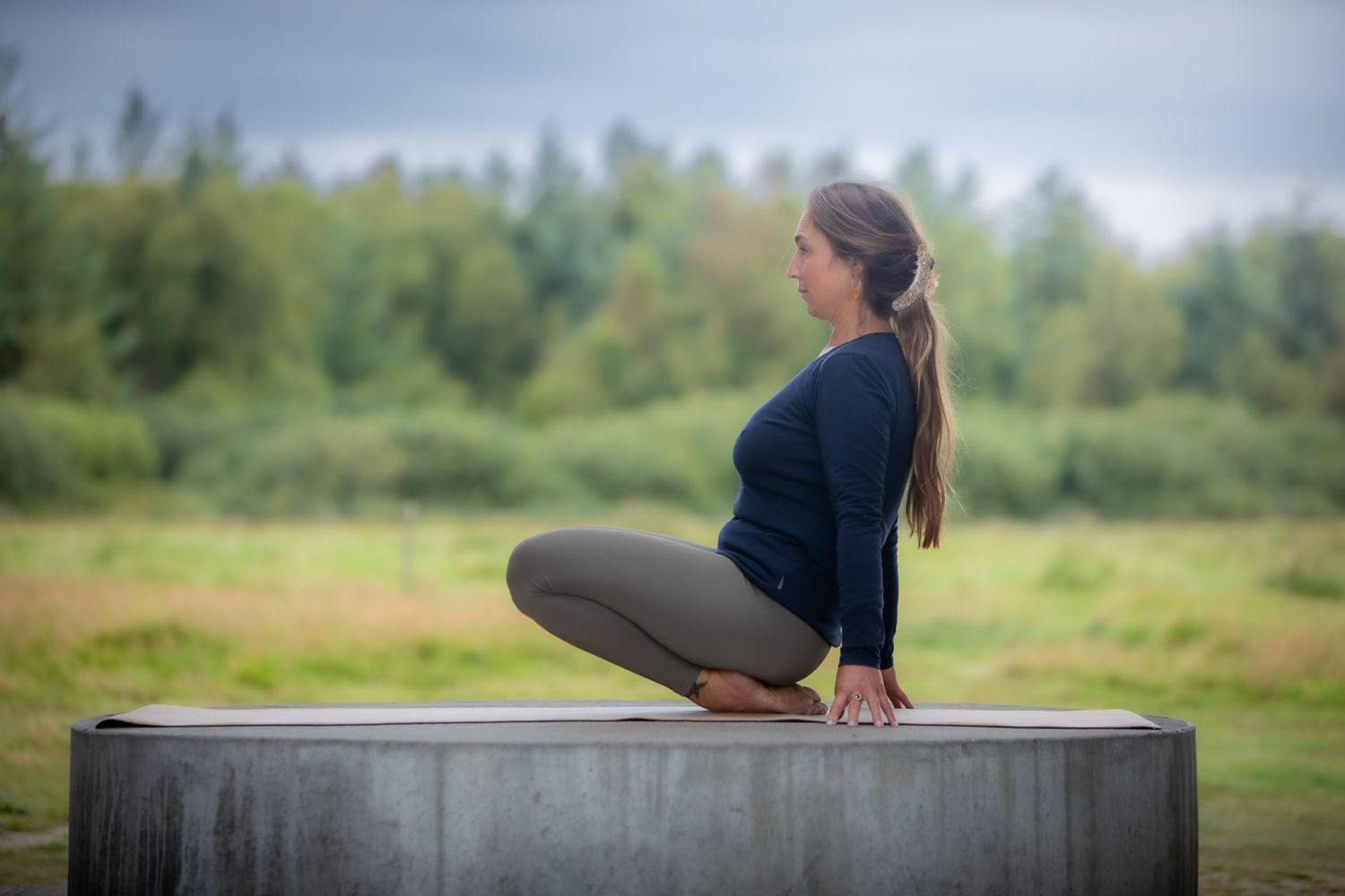 Person performing stretching exercises on concrete platform in natural outdoor setting.