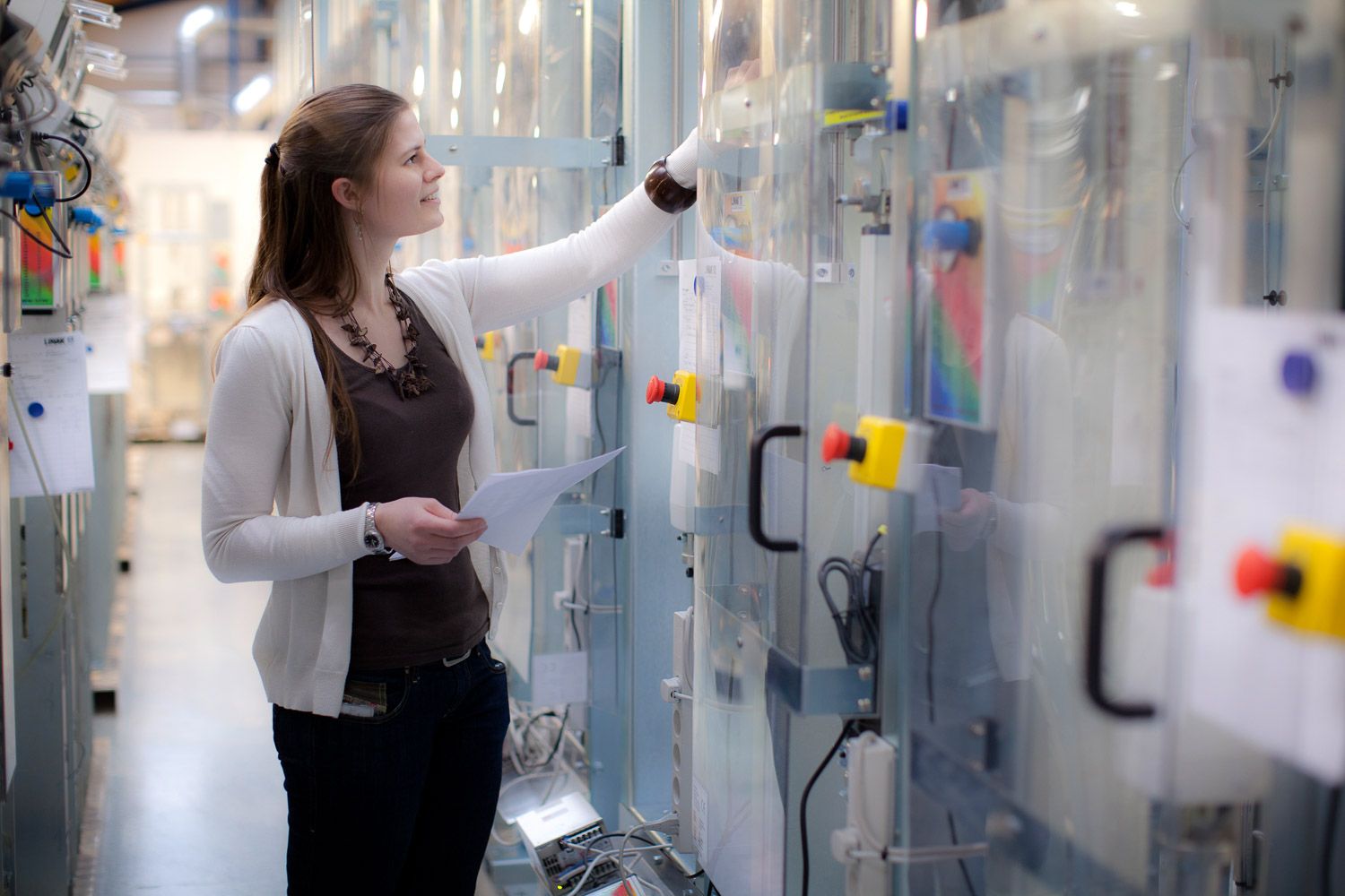 Researcher examining laboratory equipment and taking notes in scientific facility.