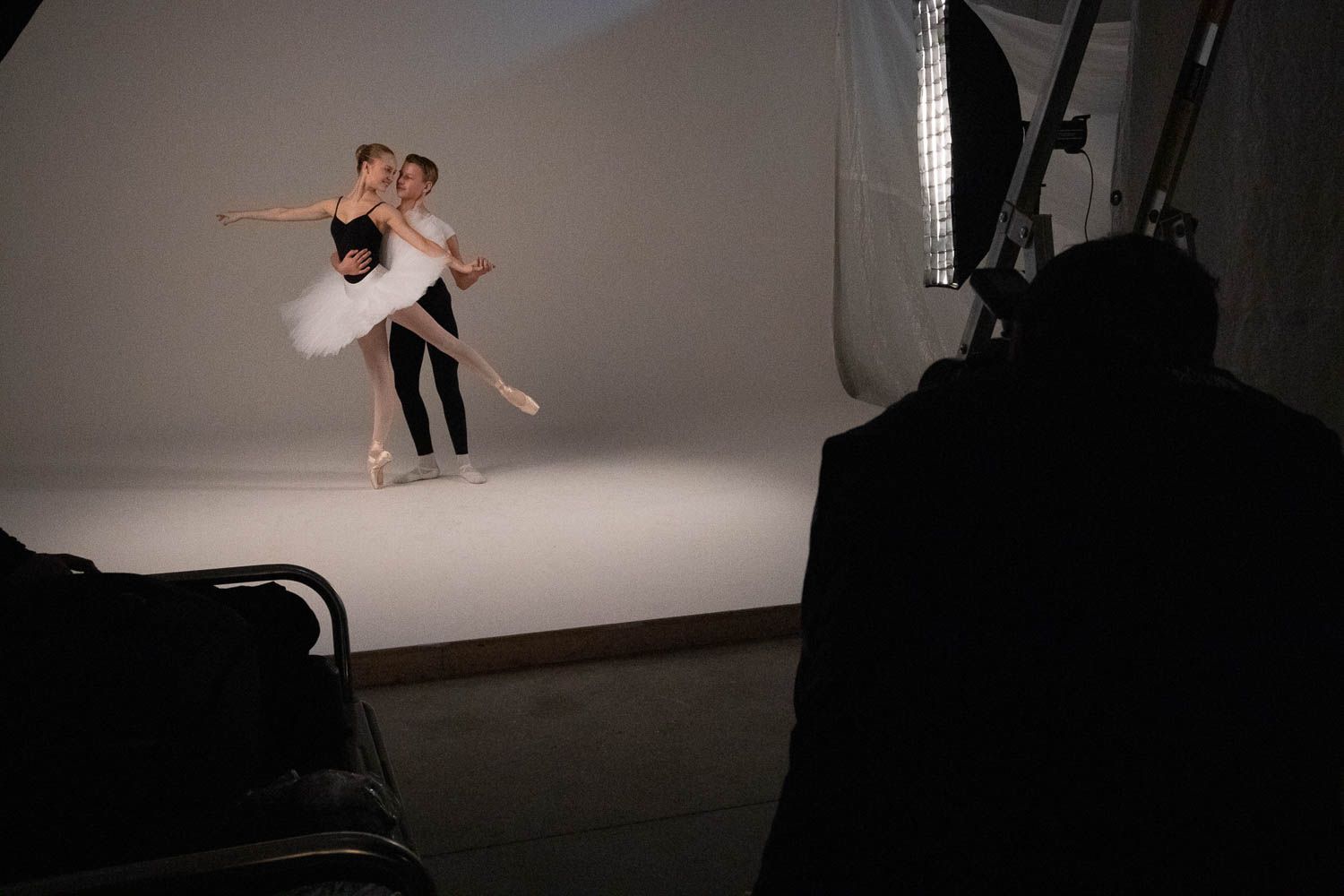 Two dancers perform a graceful lift in a photography studio setting.