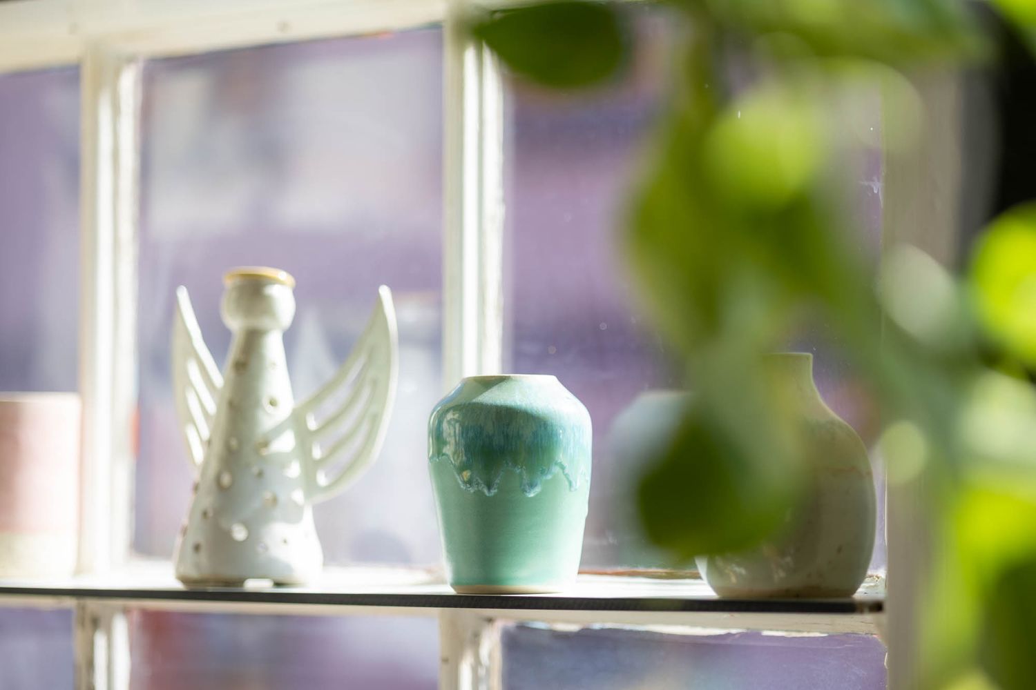 Decorative vases and ceramic pieces displayed on window shelf with soft natural lighting.