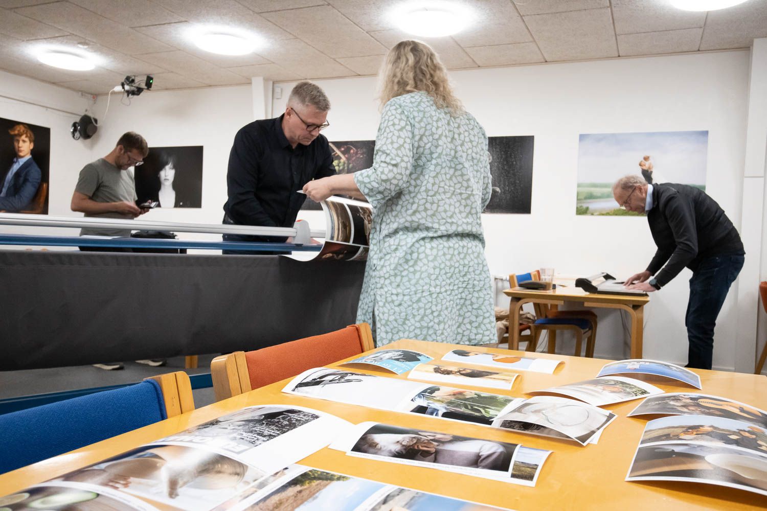 Interior of a bright meeting room with photographs laid out on an orange table for review.