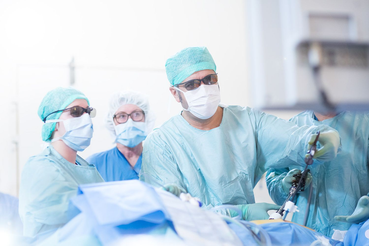 Medical team conducting surgery while wearing protective gear and surgical masks.