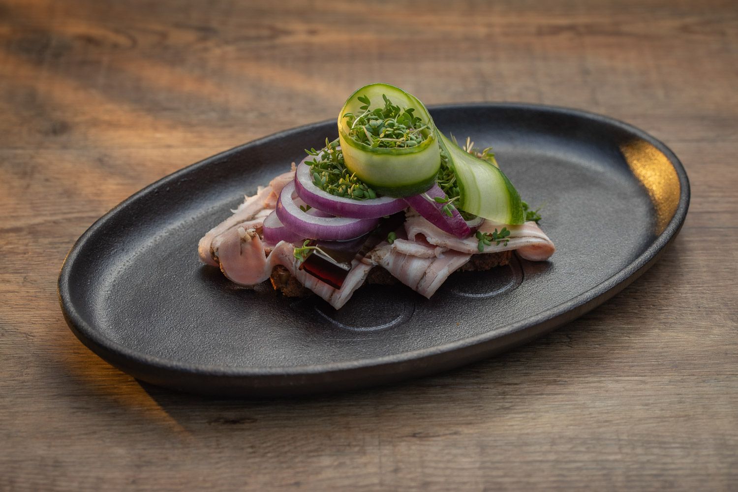 Seared tuna dish with red onions and greens served on a black plate.
