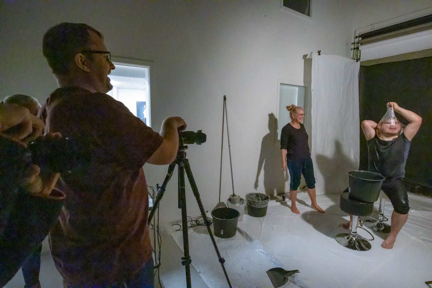 Photographer with camera on tripod captures fitness photoshoot in white studio setting.