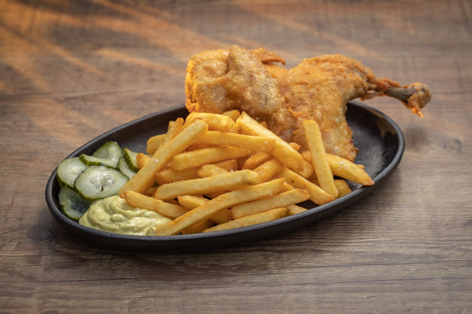Fried chicken with french fries and cucumber slices on black plate.
