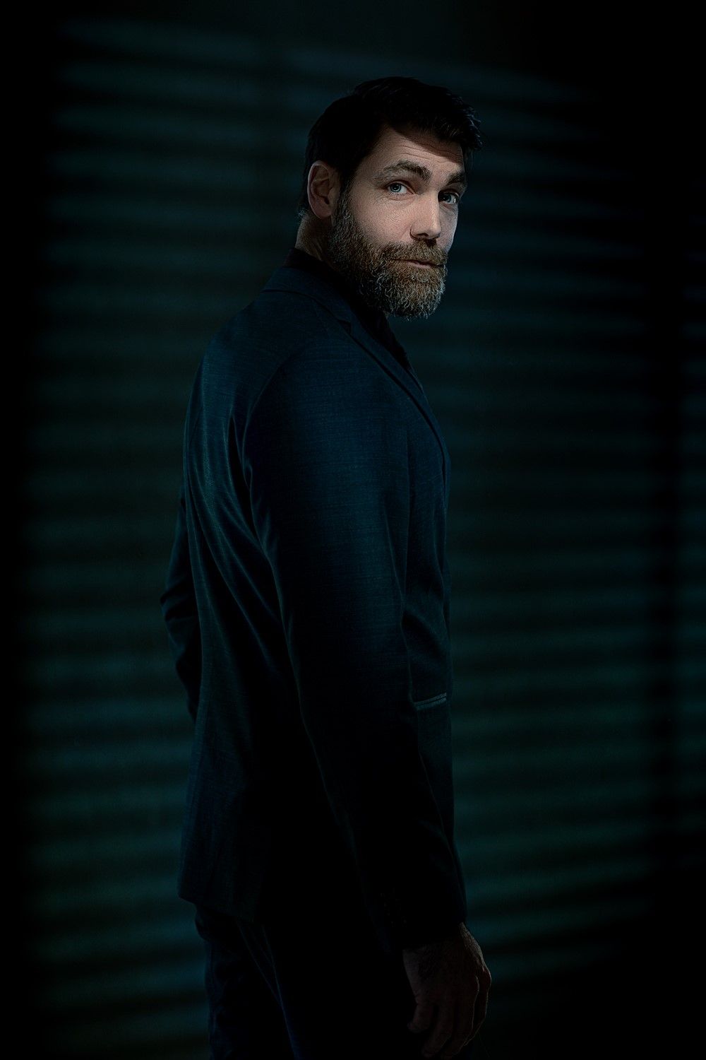 Atmospheric portrait showing person in dark clothing against shadowy background.