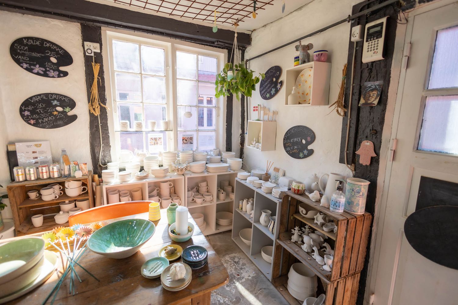 Bright ceramic studio interior with shelving displaying pottery supplies and handmade items.