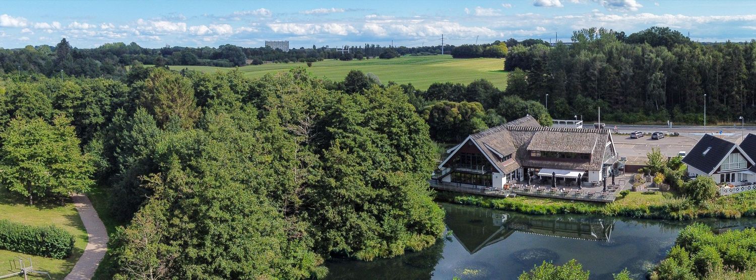 Aerial view of luxury resort buildings surrounded by lush green forest and serene lake.