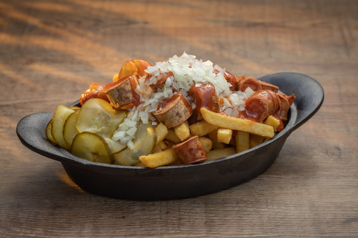 Loaded french fries topped with meat, cheese and pickles in cast iron skillet.