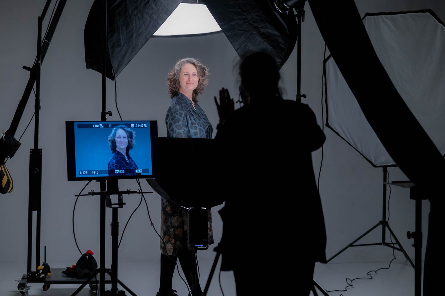 Dark studio setup with lighting equipment and monitors visible during photo shoot.