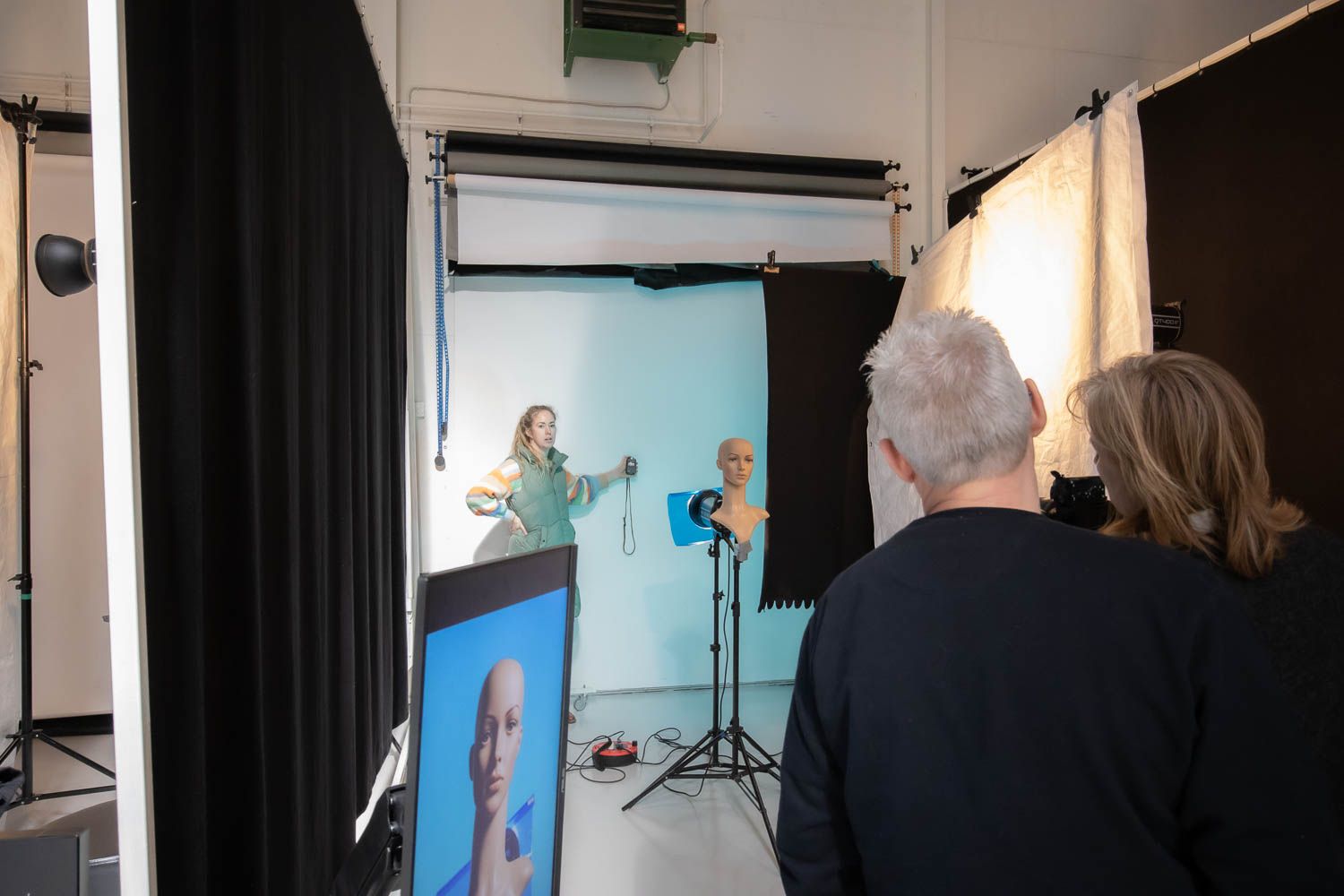 Photography team reviewing shots during studio session with blue backdrop and lighting setup.