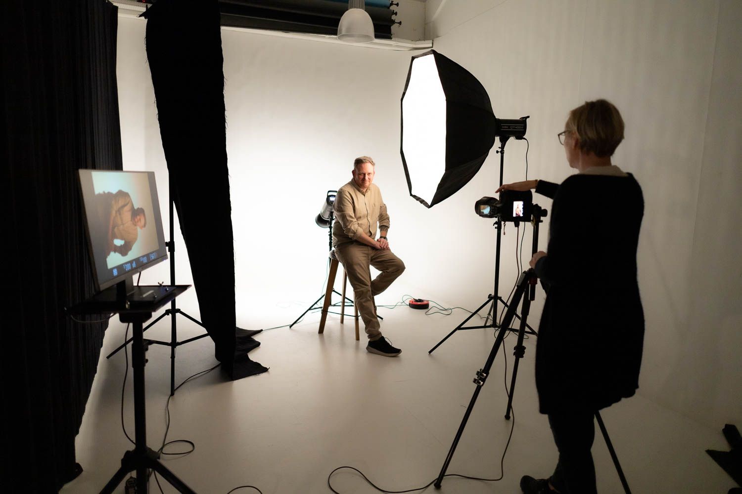 Wide angle view of a photography studio with lighting equipment and backdrop during a photo session.