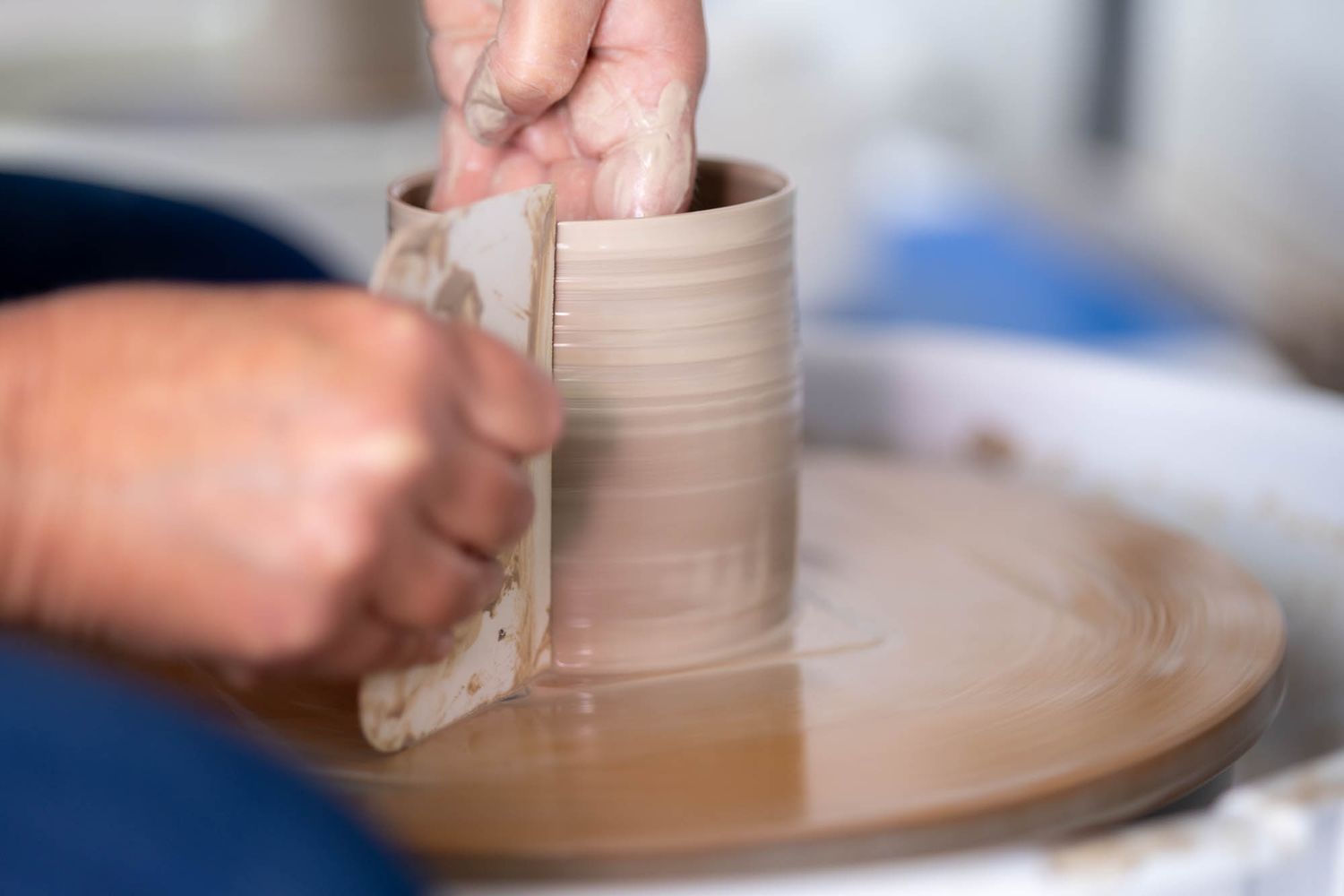 Hands carefully shape a clay vessel on a spinning pottery wheel.
