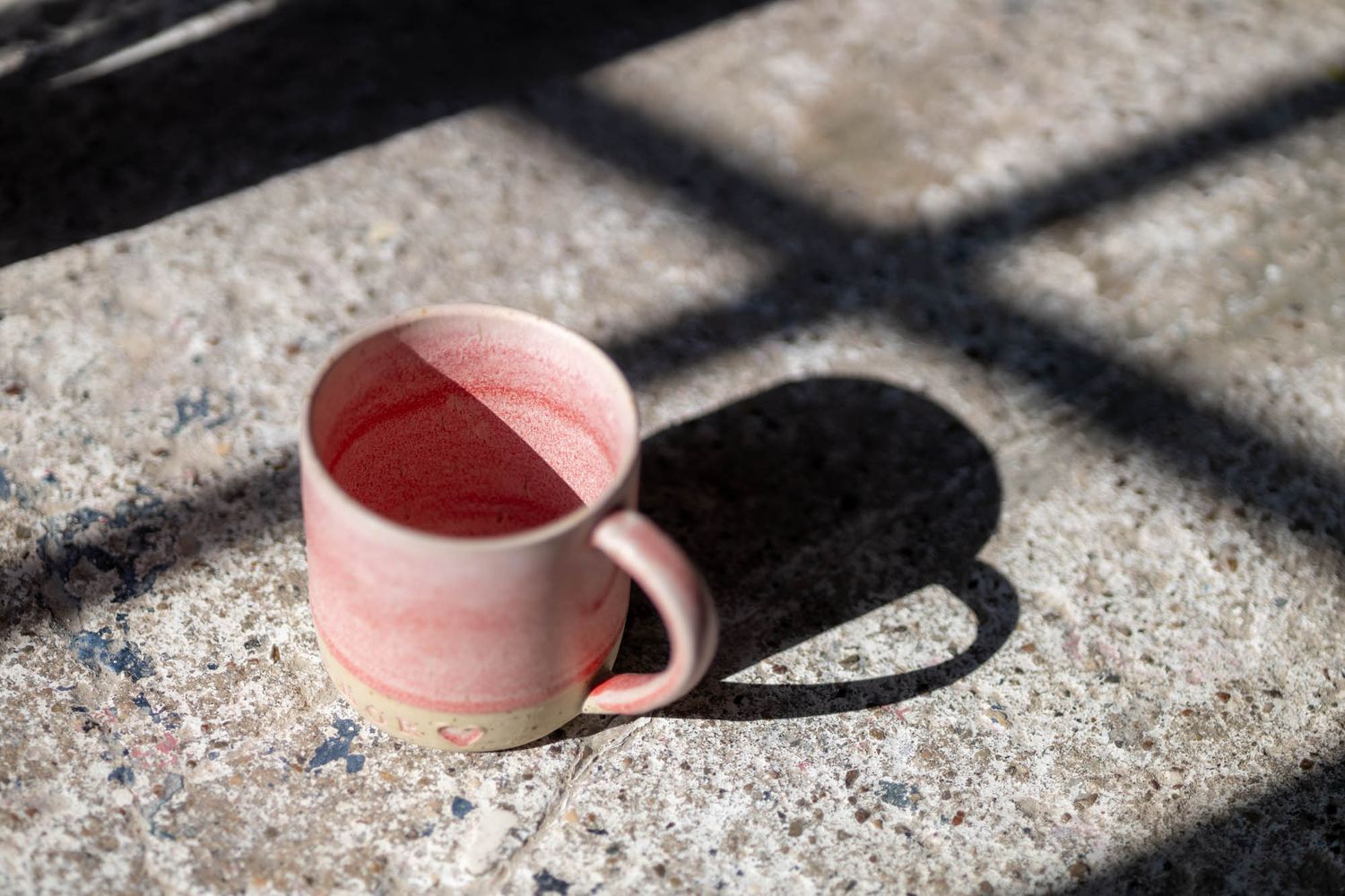 Pink ceramic mug on concrete surface with dramatic shadow in sunlight.