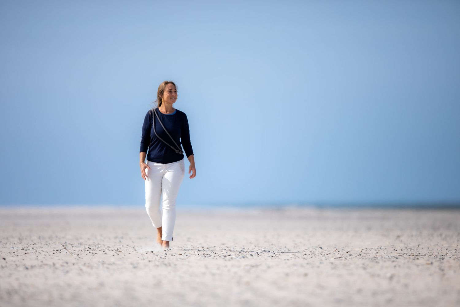 Walking along a sandy beach with clear blue skies in the background.
