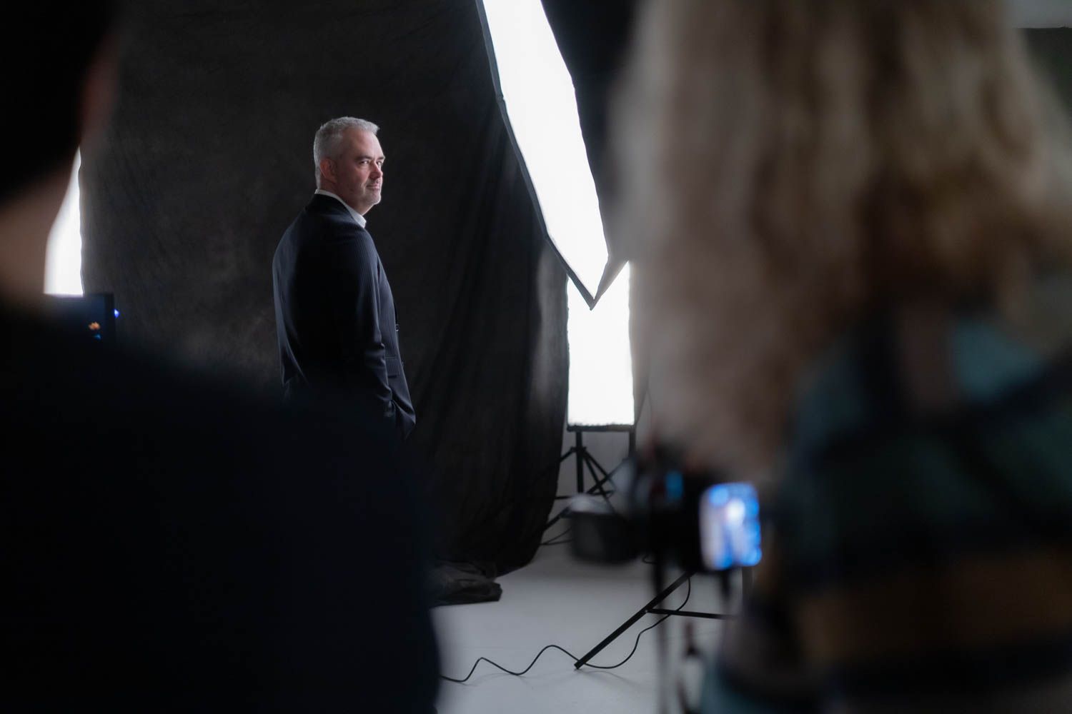 Dark studio setting with dramatic lighting and photography equipment silhouettes.