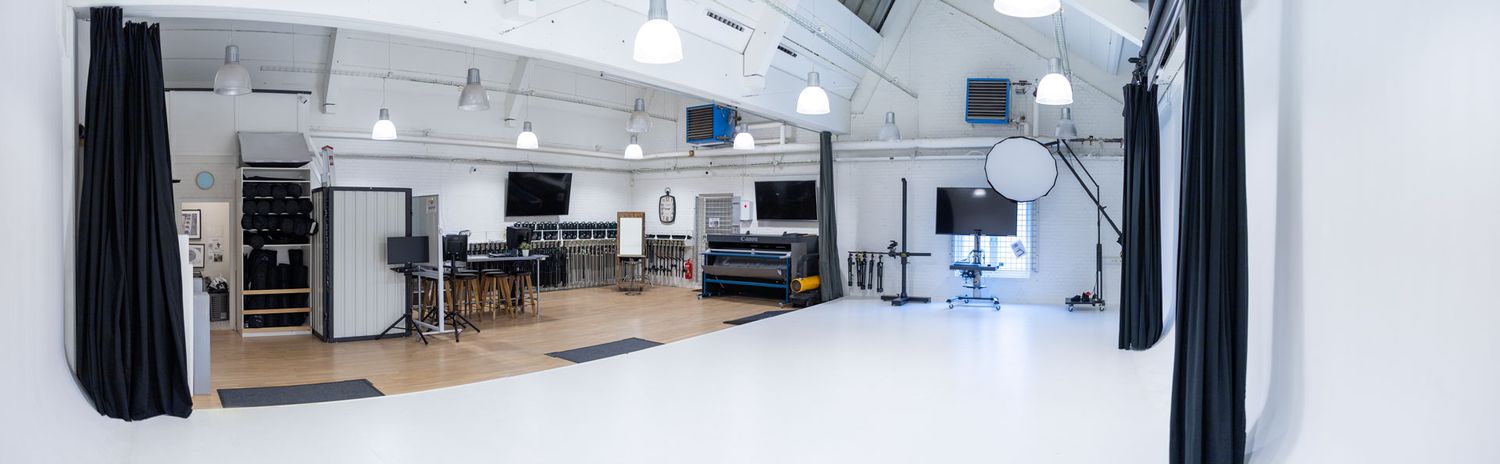Modern white photography studio interior with lighting equipment and workstations.