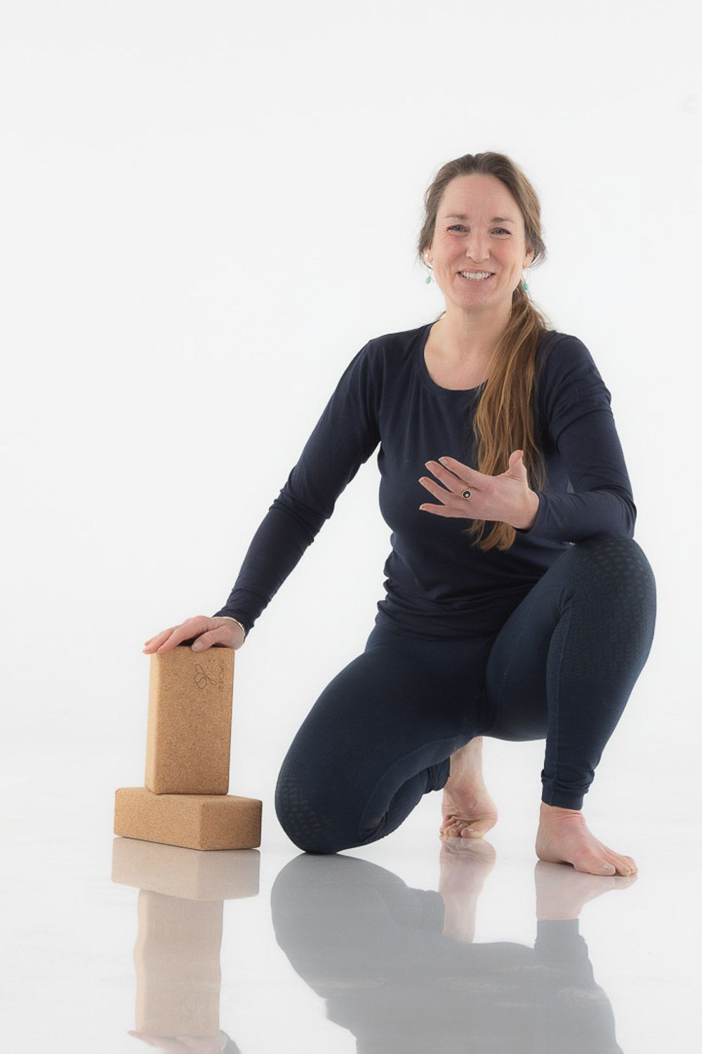 Person in black athletic wear kneeling beside cork yoga blocks on reflective surface.